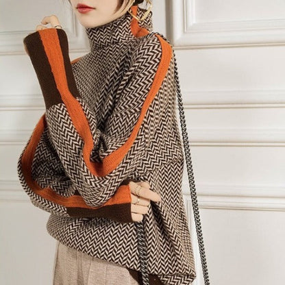 Close-up of the brown herringbone jumper worn with arms crossed, showing orange stripes along the sleeves, brown cuffs and a chain bag strap. 3