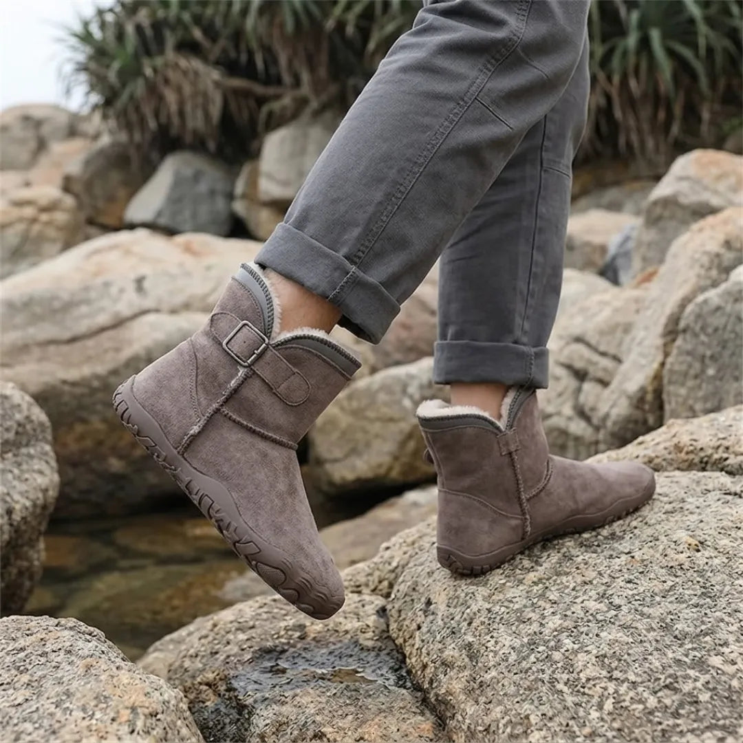 Person in rolled-up grey trousers wearing taupe fleece-lined boots while walking over coastal rocks 38