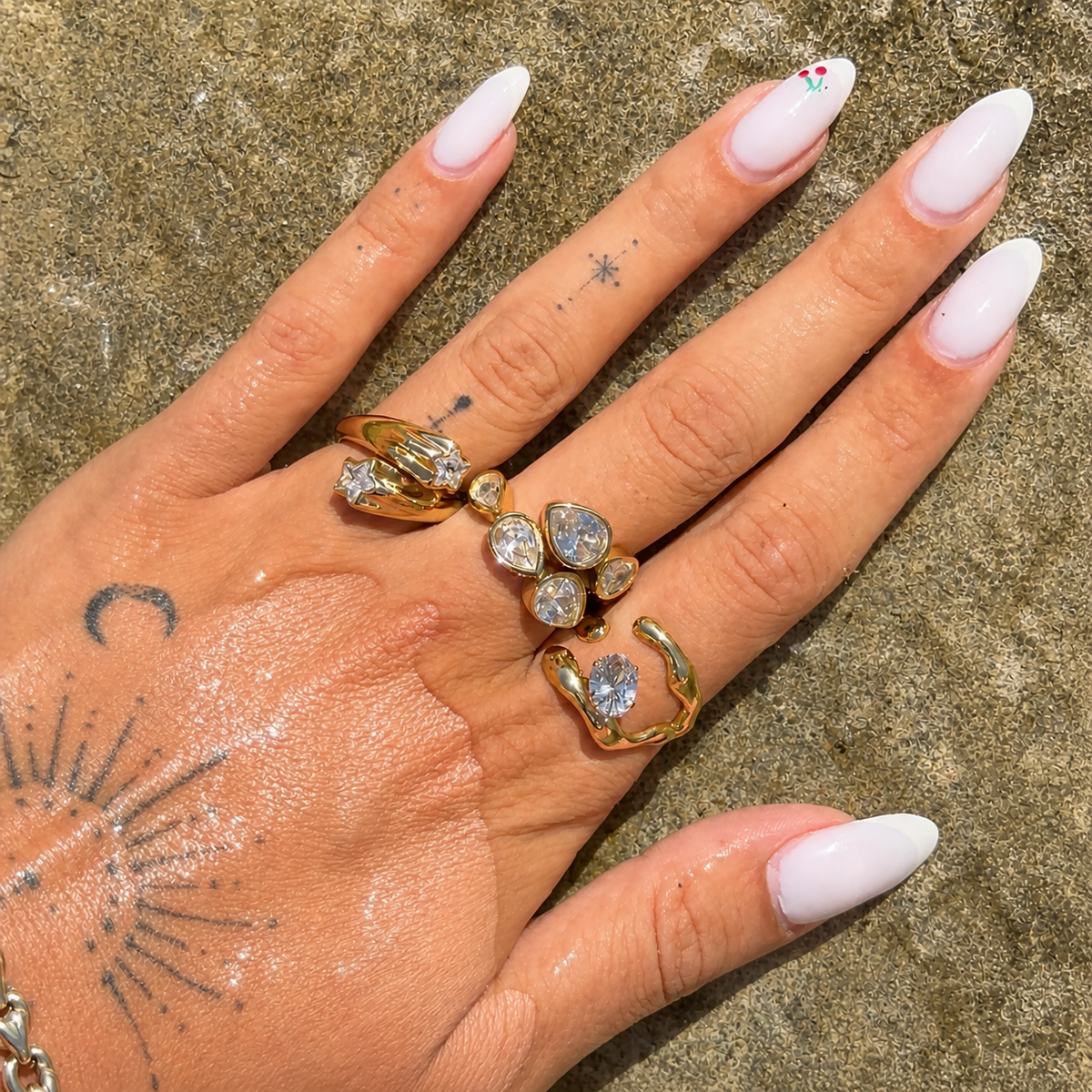 Hand with white almond nails wearing the open gold-tone ring with its oval stone, stacked with other stone-set gold rings. 3