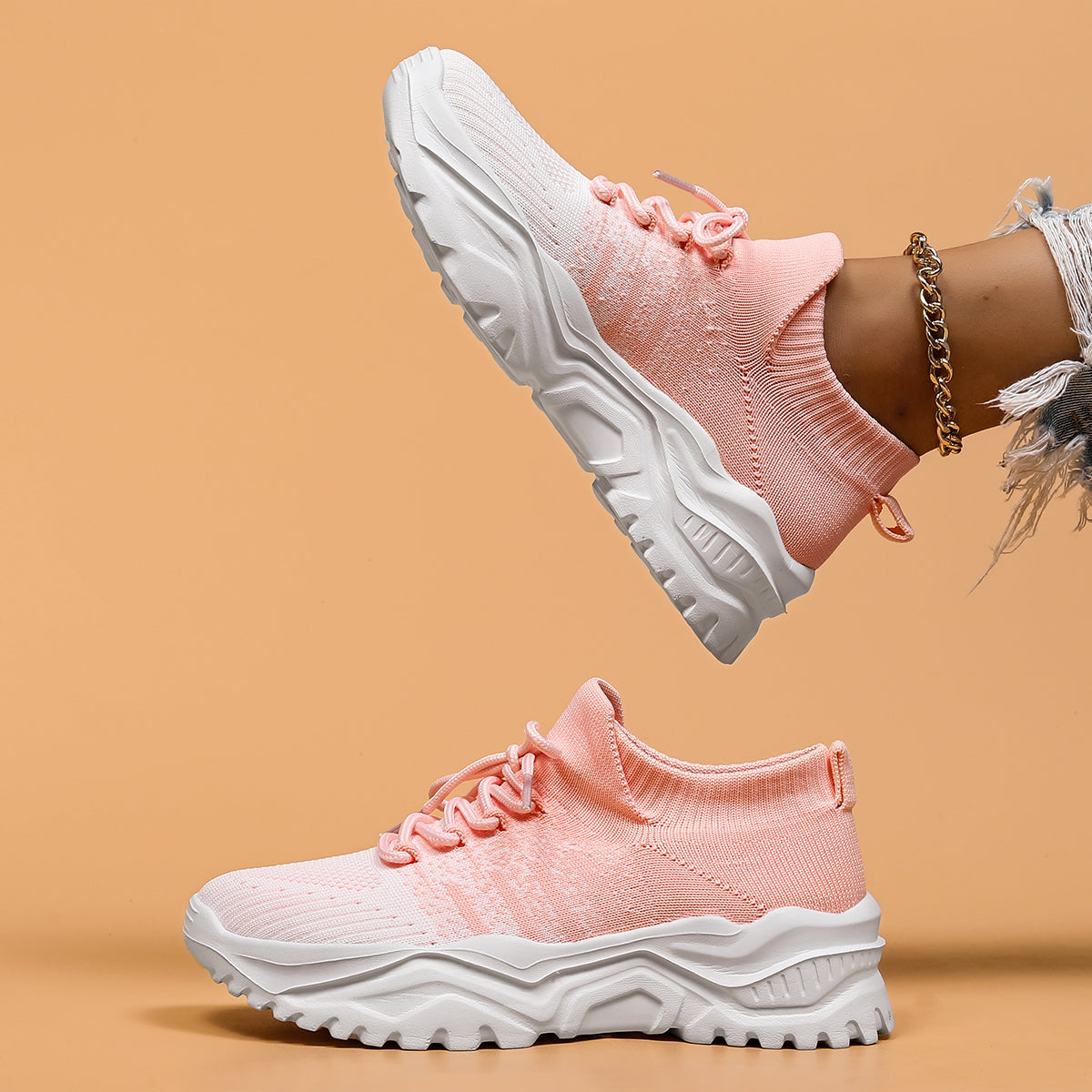 Side view of pink and white gradient knit sneakers with thick white treaded soles, one shoe lifted above the other. 5