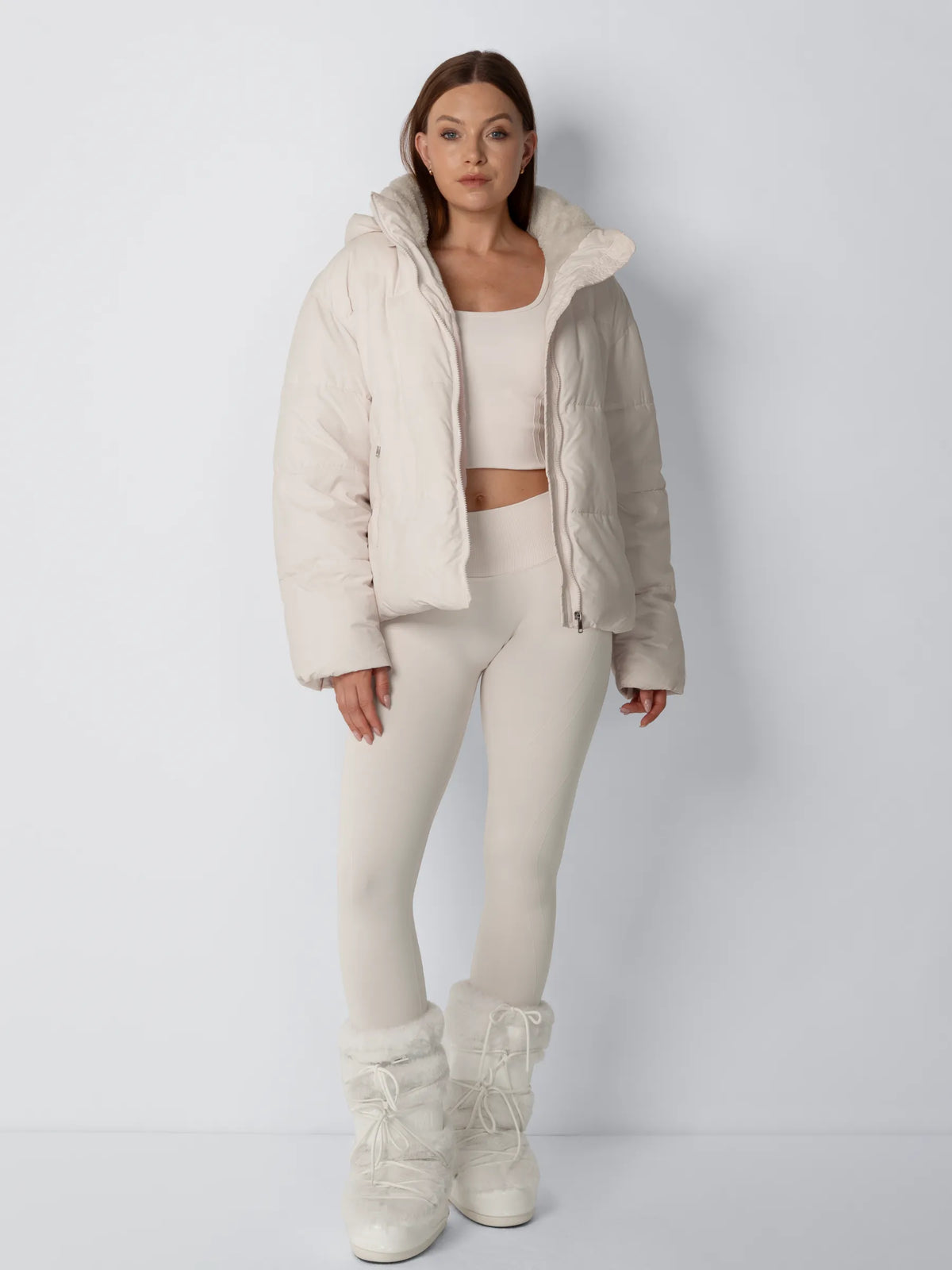 Full-length front view of a cream puffer jacket worn unzipped with a cream crop top, leggings and fluffy boots 5