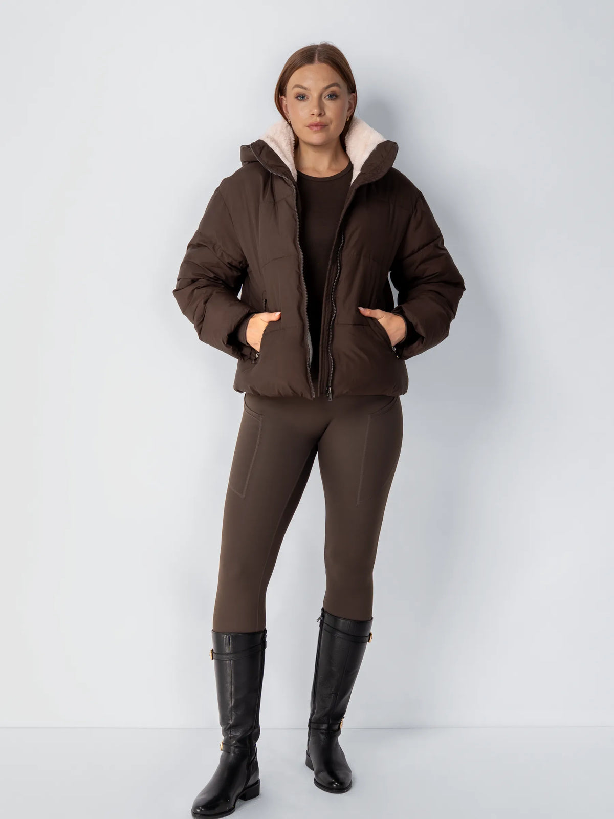 Full-length view of a dark brown puffer jacket styled with brown leggings and tall black boots 15