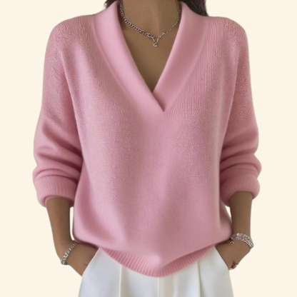 Model wearing the relaxed V-neck knit in soft pink with white trousers, silver necklace and bracelets, hands in pockets. 2
