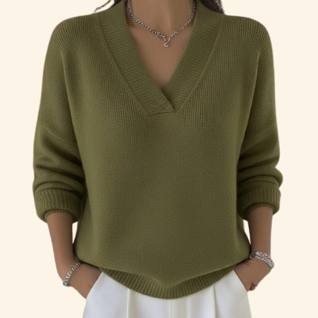 Model wearing the ribbed V-neck knit in olive green with white trousers, silver necklace and bracelets, hands in pockets. 3