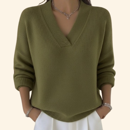 Model wearing the ribbed V-neck knit in olive green with white trousers, silver necklace and bracelets, hands in pockets. 3
