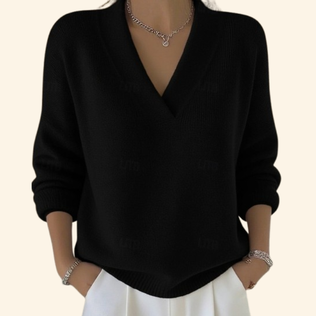 Model wearing the long-sleeved V-neck knit in black with white trousers, silver necklace and bracelets, hands in pockets. 4