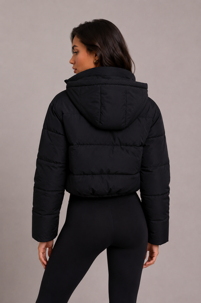 Back view of the black quilted puffer jacket on a model, showing the horizontal quilting, the hood folded down and the cropped hem. 4