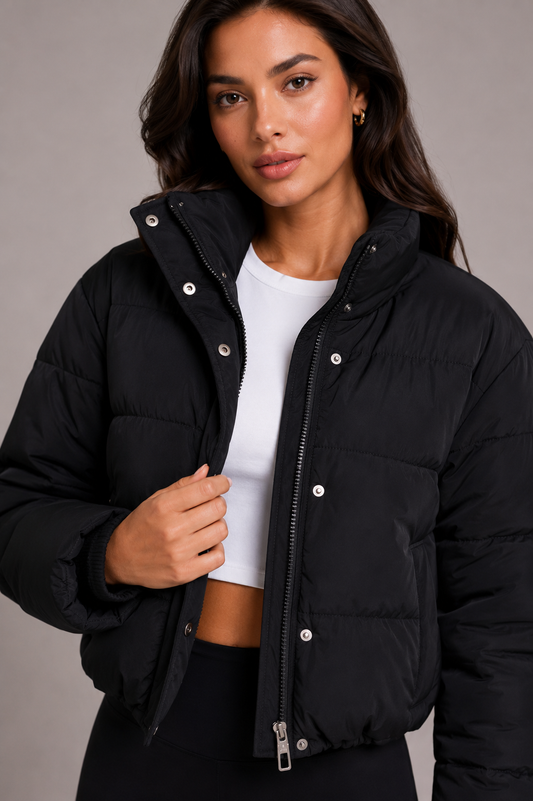 Close-up of the black quilted puffer jacket worn open over a white crop top, showing the zip, press studs and high collar. 1