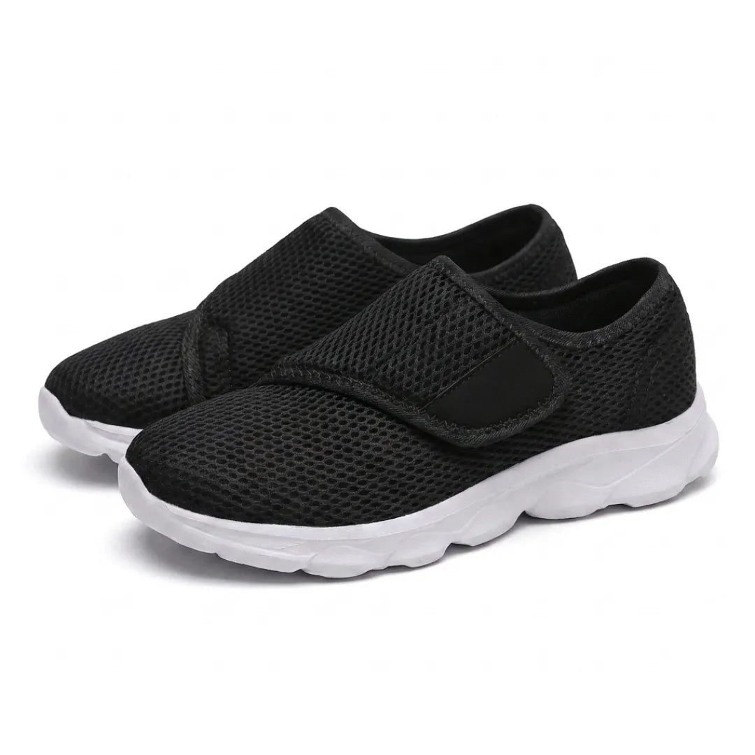 Pair of black mesh shoes with white soles and hook-and-loop straps, seen from the front three-quarter 25