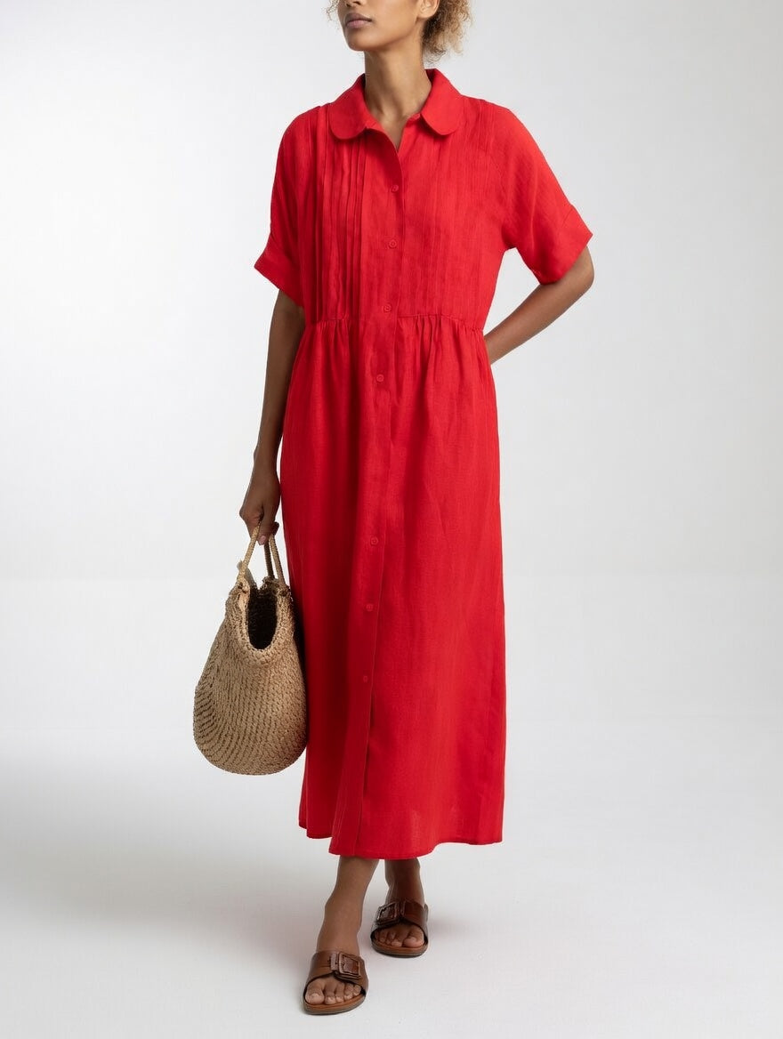 Model in the red dress, hand behind her back, holding a straw tote, showing the pleated chest and button front. 5