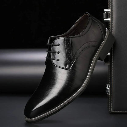Single black polished lace-up shoe with brogue perforations and contrast stitching, shown side-on against a dark briefcase. 3