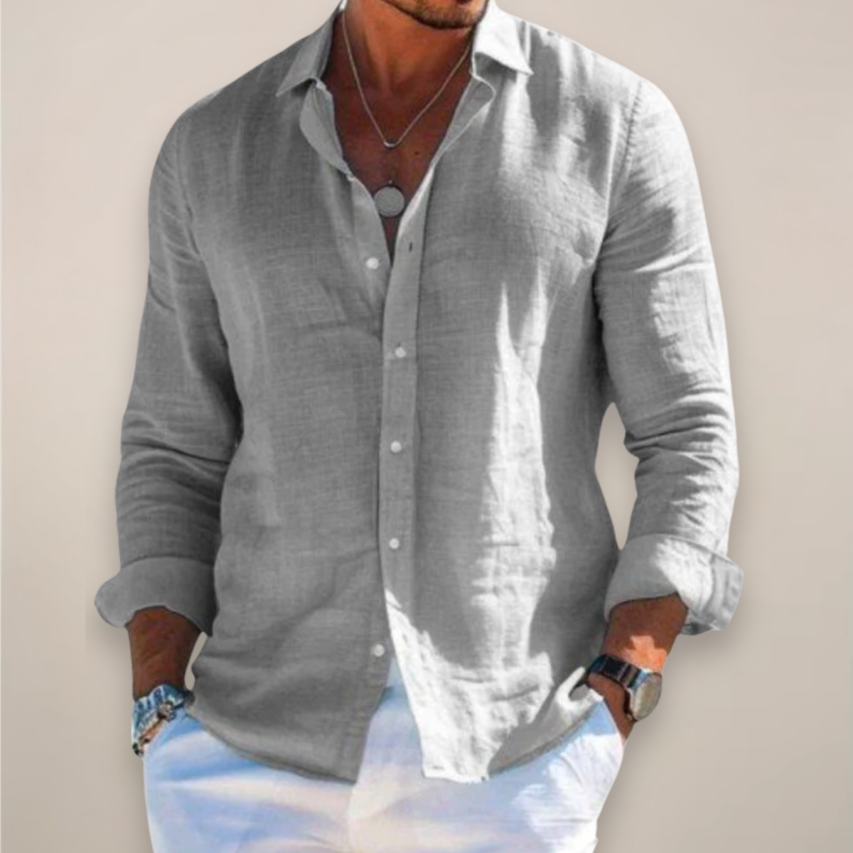 Model wearing the grey version of the shirt, buttoned with sleeves rolled up, hands in pockets of white trousers. 1