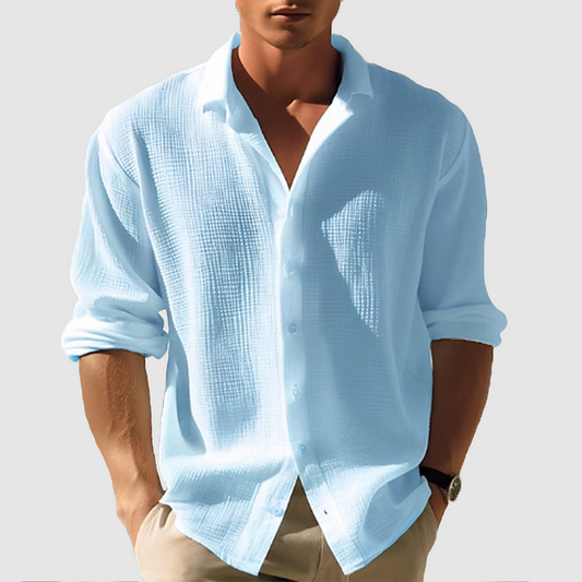 Model wearing the textured shirt in light blue, sleeves rolled, hands in beige trouser pockets 1