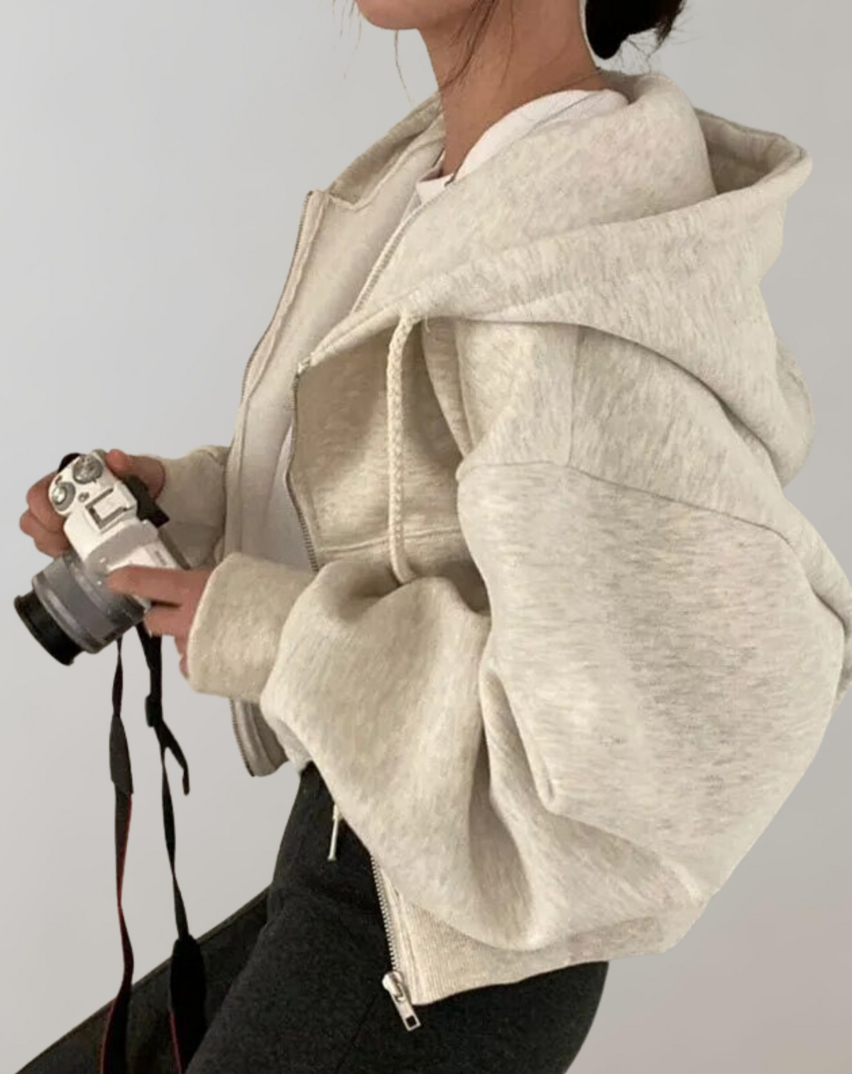 Side view of a light grey marl hoodie on a model holding a camera, showing the roomy hood and full sleeves. 2