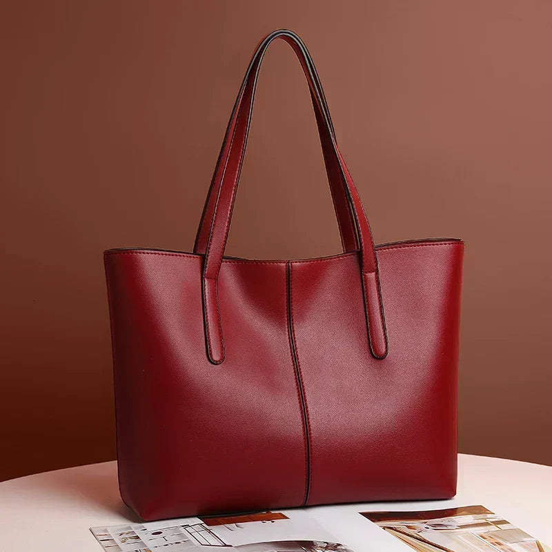 Deep red tote bag angled on a white table against a brown wall, resting on a magazine 3
