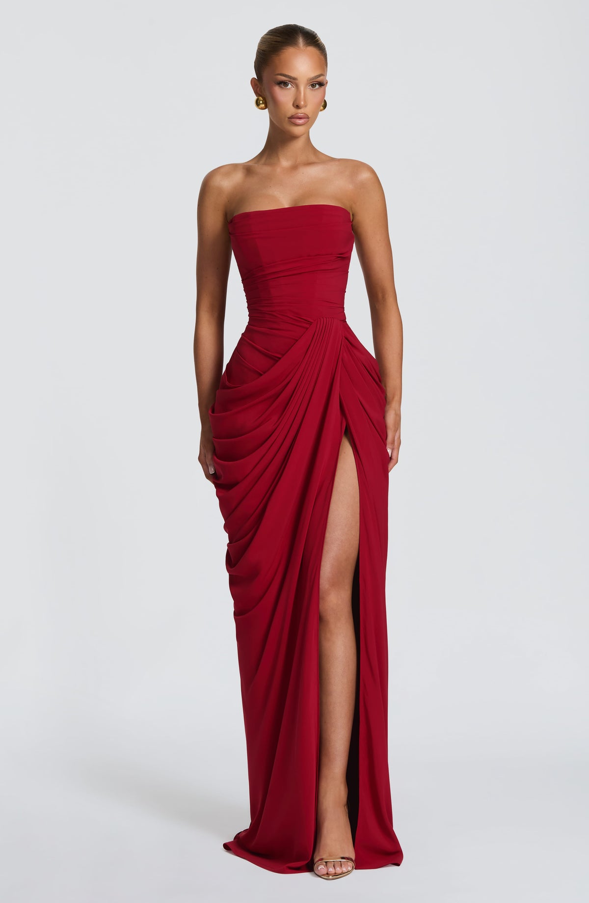 Full-length front view of the red dress on a model, the high slit revealing one leg, worn with gold heels. 30
