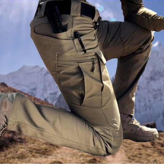 Model in khaki cargo trousers kneeling on a mountain slope, showing the zipped thigh pocket and a pen clipped to the upper pocket. 1