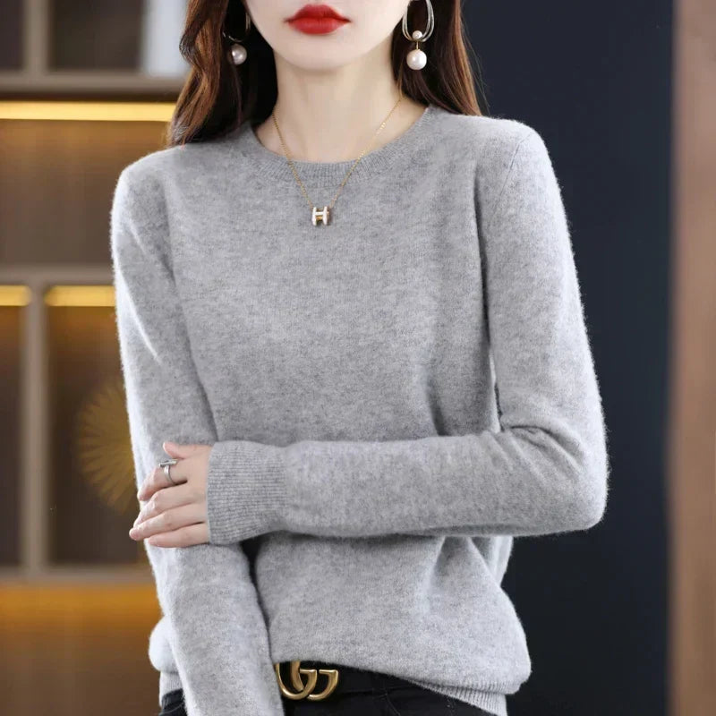 Model wearing the jumper in light grey with black trousers and a belt, hands clasped 20