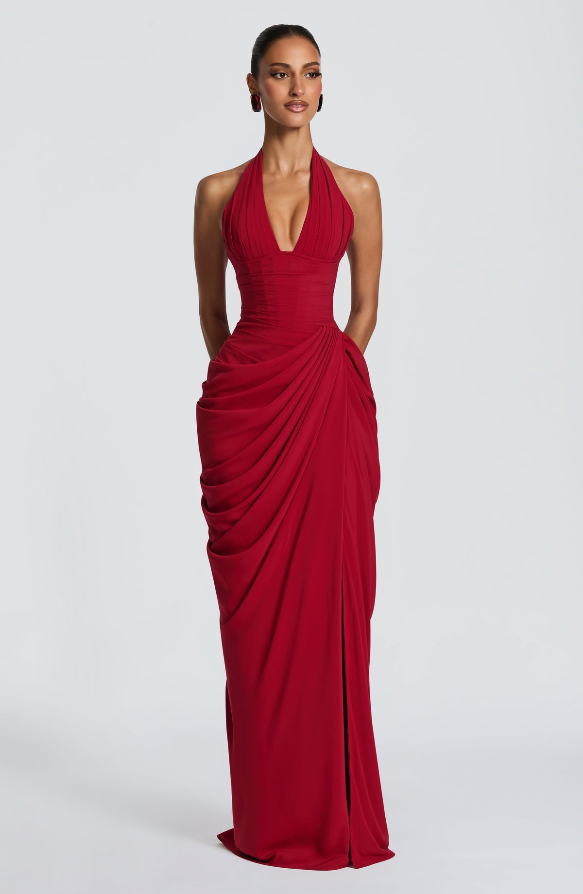 Model faces the camera in the red halterneck maxi dress, showing the pleated plunging bodice, corset waist and draped chiffon skirt. 21