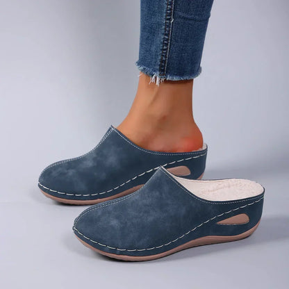 Blue backless wedge slippers worn with frayed jeans, side view showing the fleece lining, white stitching and teardrop cut-out in the sole. 4