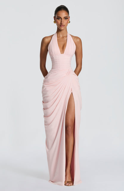 Model facing forward in the pale pink halterneck maxi dress, showing the pleated plunge neckline, corset waist and draped skirt with high slit. 1