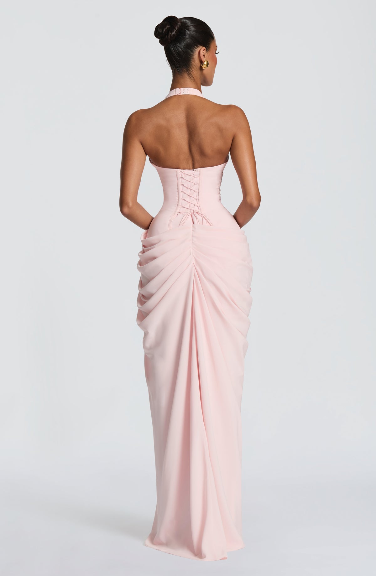 Back view of the pale pink dress showing the lace-up corset back, halter fastening and gathered, ruched skirt drape. 2