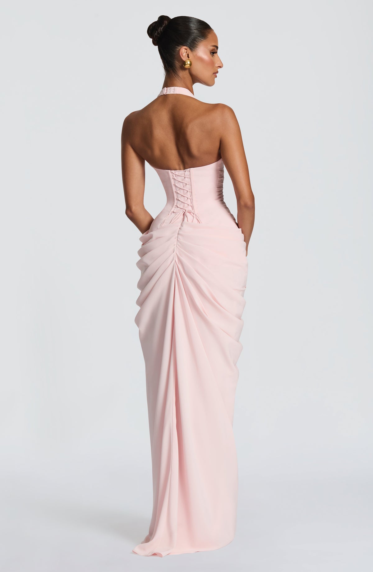 Back view of the pale pink dress showing the corset lacing and ruched skirt, with the model's head turned slightly to the side. 7