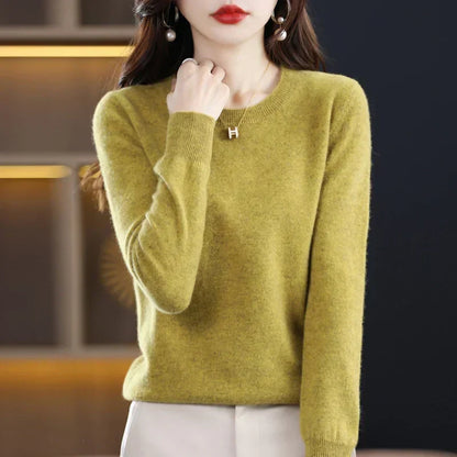Model wearing the jumper in olive-green with cream trousers, one hand raised to her collar 13