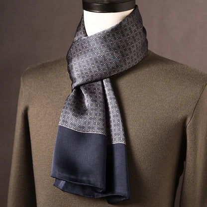 Grey and navy silk scarf with a fine geometric maze-like pattern and plain navy ends, draped on a mannequin over an olive jumper. 10