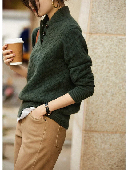 Side view of a model in the dark green cable-knit sweater with white shirt underneath, tan trousers and a takeaway coffee cup. 8
