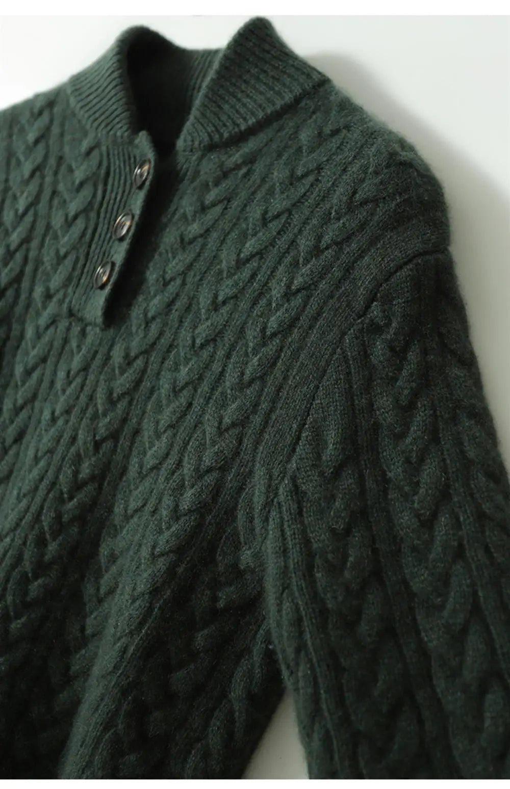 Angled close-up of the dark green cable-knit sweater showing the braided cable pattern across the body and sleeve, with the buttoned collar. 20