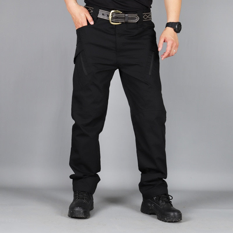 Front view of black trousers worn with a belt, watch and black boots, one hand resting in the side pocket. 5