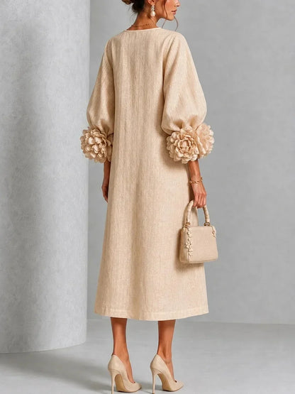 Back view of the beige dress on a model, showing the plain textured back, loose A-line fall and large flower decorations on the sleeve cuffs. 7