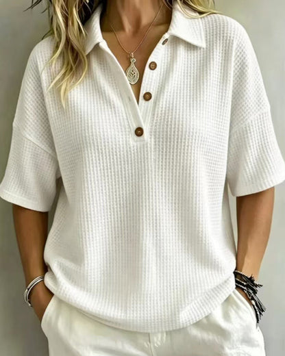 White waffle knit polo top with three wooden buttons, worn with white trousers and a pendant necklace 1