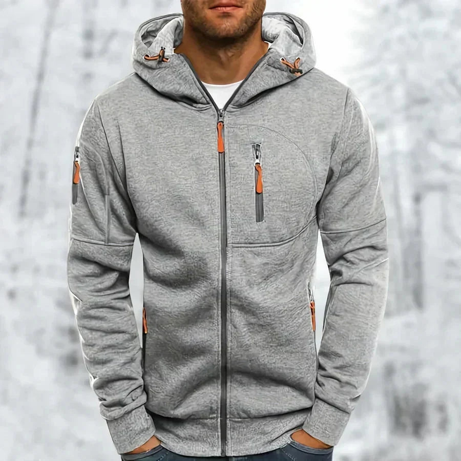 Model wearing the hoodie in light grey with a subtle textured jacquard finish and orange zip pulls, against a snowy background. 8