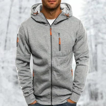 Model wearing the hoodie in light grey with a subtle textured jacquard finish and orange zip pulls, against a snowy background. 8