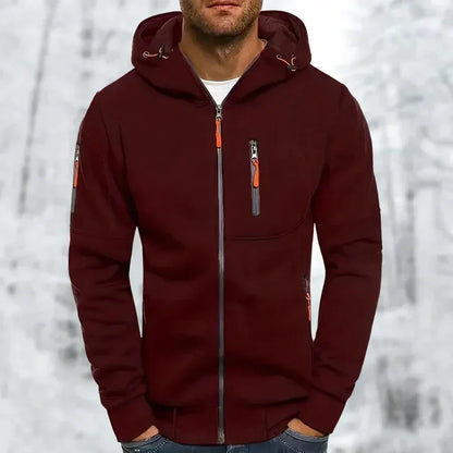 Model wearing the hoodie in dark burgundy with orange zip pulls and grey zip tapes, standing in a wintry setting. 4