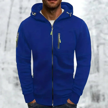 Model wearing the zip-up hooded top in royal blue with lime green zip pulls, hands in pockets, against a wintry backdrop. 1