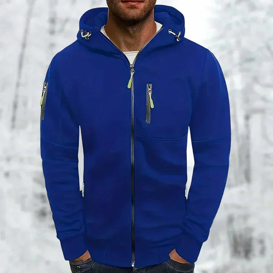 Model wearing the zip-up hooded top in royal blue with lime green zip pulls, hands in pockets, against a wintry backdrop. 1