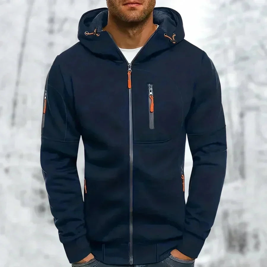 Model wearing the hoodie in navy blue with orange zip pulls, chest zip pocket and sleeve pocket, against a snowy background. 5