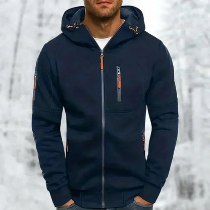 Model wearing the hoodie in navy blue with orange zip pulls, chest zip pocket and sleeve pocket, against a snowy background. 5