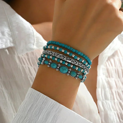Wrist wearing the stack of five bracelets, viewed from above, showing the oval turquoise stones and engraved silver-tone bangle. 2