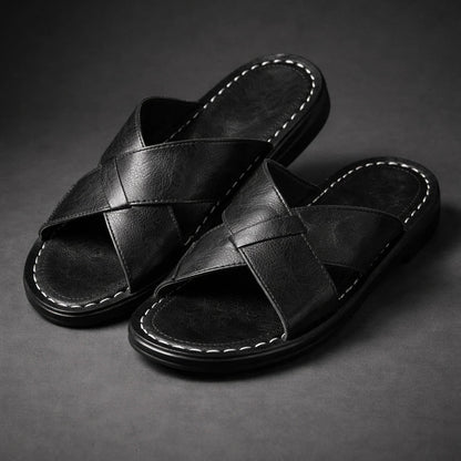 Pair of black crossed-strap slip-on sandals with white contrast stitching round the footbed, shown at an angle on a grey backdrop. 2