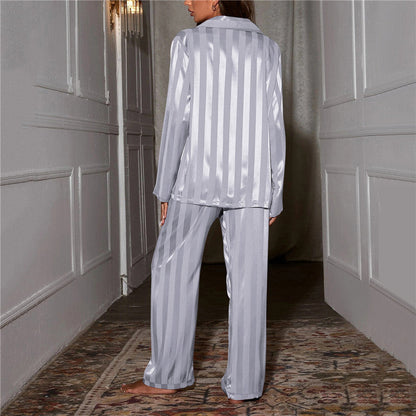 Back view of grey striped satin pyjamas worn by a model standing in a hallway 10