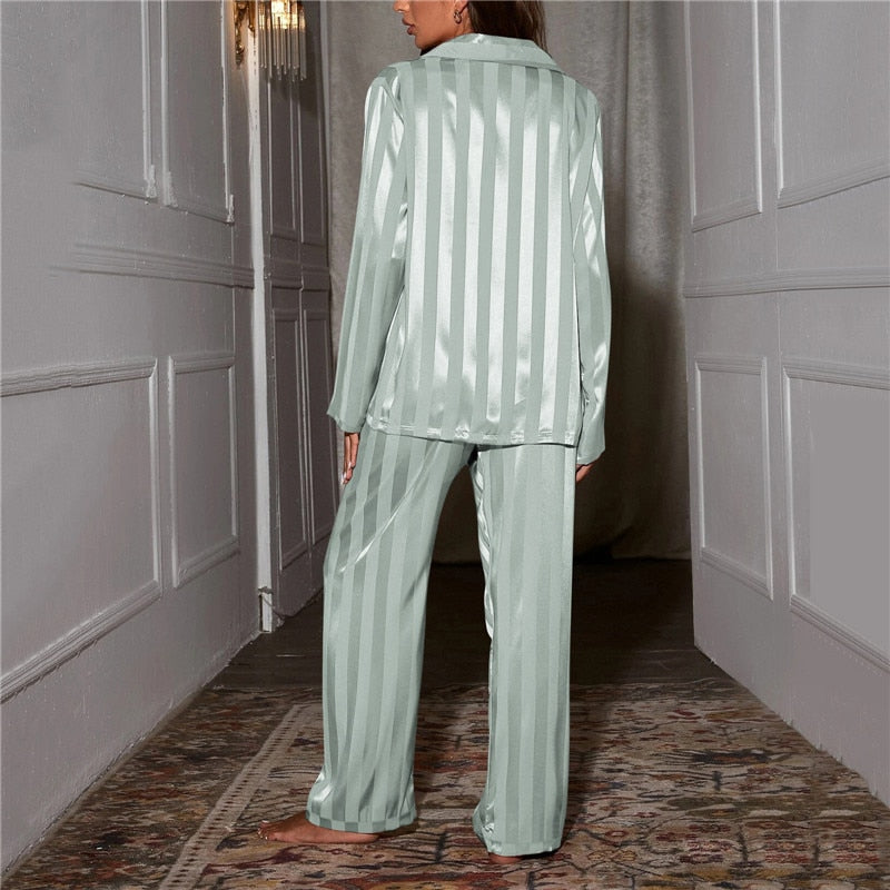 Back view of pale green striped satin pyjamas worn by a model standing in a hallway 13