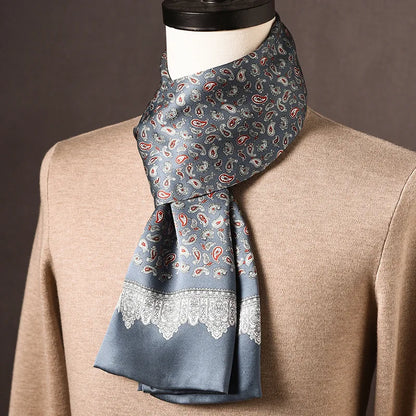 Grey-blue silk scarf with red and white paisley print and a white lace-like border, draped on a mannequin over a beige jumper. 18