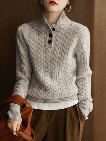 Model in the light grey cable-knit sweater with three dark buttons, white layer at the hem and brown trousers, holding a leather bag. 14