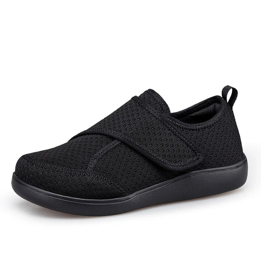 Black breathable mesh shoe with wide hook-and-loop strap and black sole, seen from the front side 1