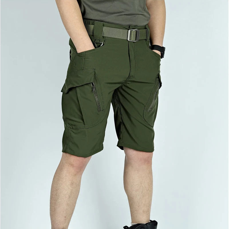 Man wearing olive green cargo shorts with a belt, one hand in a pocket, showing the flapped zip pockets from the front. 7