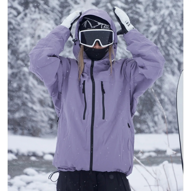 Model in a lilac hooded jacket with black zips, raising both gloved hands to the hood in falling snow. 1